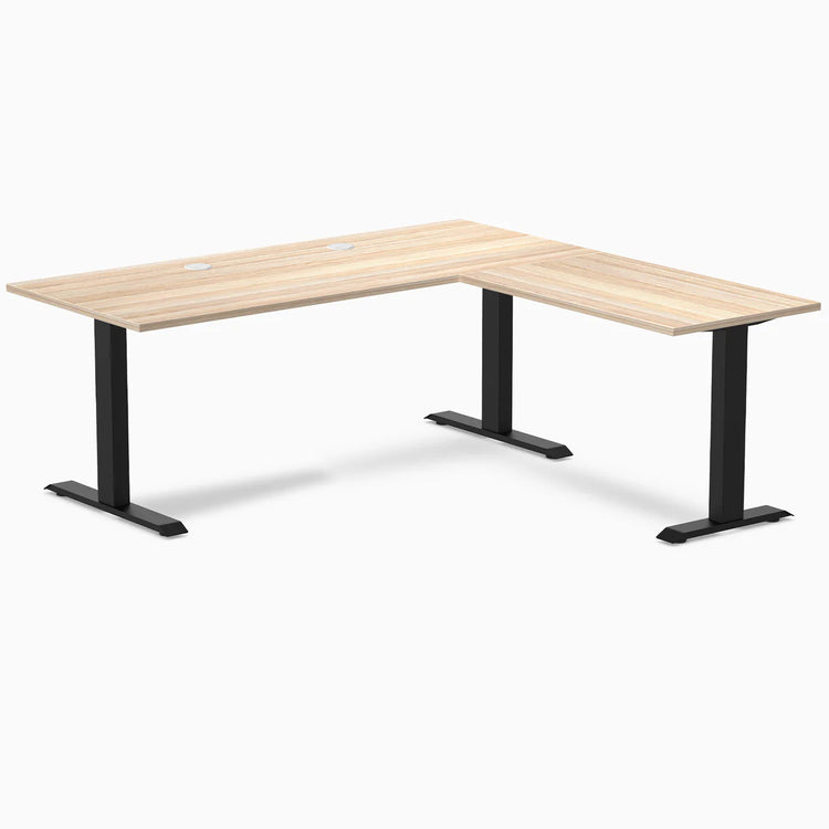 Desky Zero L-shape office desk in classic oak laminate with matte black steel frame and grommets.