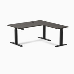 Desky L-Shape Laminate Sit Stand Desk in burnished wood with matte black legs and grommets.
