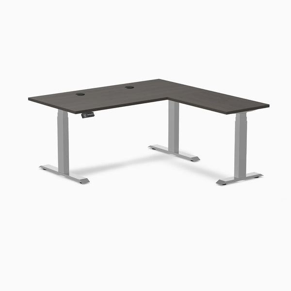 Desky L-Shape Laminate Sit Stand Desk in Burnished Wood with Gray frame and grommets.