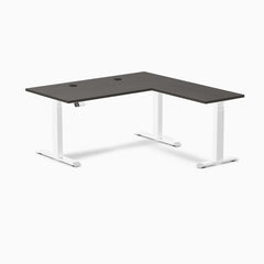 Desky L-Shape Laminate Sit Stand Desk in Burnished Wood with white legs and grommets.