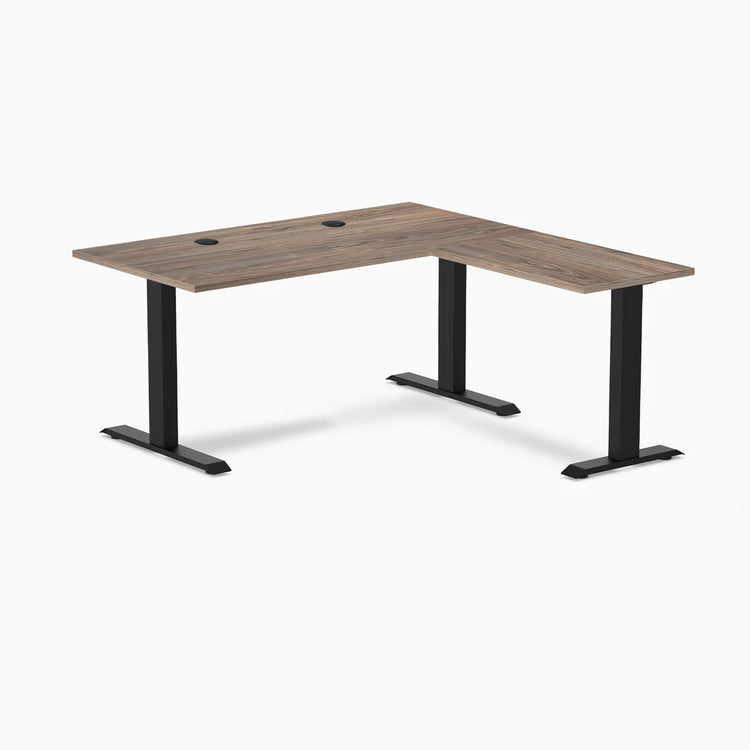 Desky Zero L-shape office desk in natural walnut laminate with matte black steel frame and grommets.