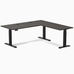 Burnished Wood L-shape laminate sit-stand desk with matte black legs and grommets.