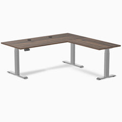 Desky L-Shape Laminate Sit Stand Desk with Jarrah Legno top, gray legs, and grommets.