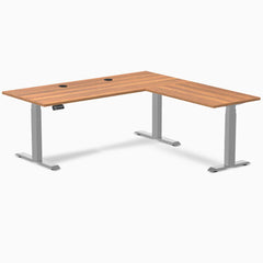 Prime Oak laminate L-shape sit-stand desk with gray frame and grommets.