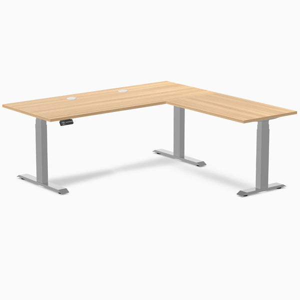 Sublime Teak L-Shape laminate sit-stand desk with gray frame, grommets, and control panel.