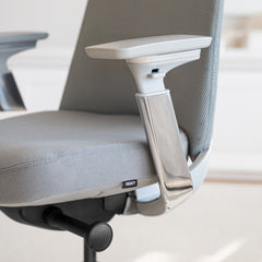Close-up of a light grey Desky Pinnacle executive office chair with mesh back, fabric seat, and polished aluminum armrests.