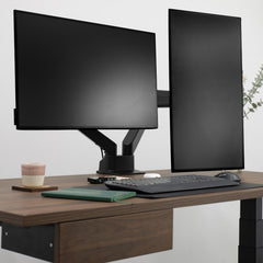 Black Desky Dual Monitor Arm supporting two screens on a dark wood desk with a keyboard and notebook.