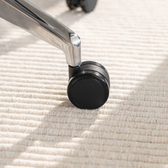 Chrome die-cast aluminum base and black caster wheel of a Desky Pinnacle office chair on a textured rug.