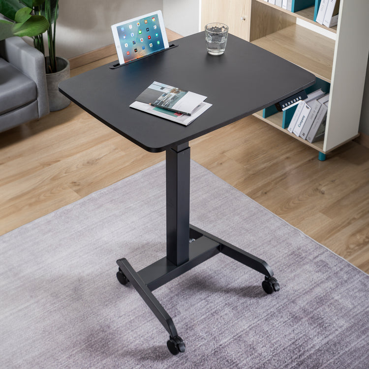 Desky Single Sit Stand Pedestal Desk in living room with gadgets on top