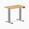 Compact Desky Dual Mini sit-stand desk with maple hardwood top, gray frame, and digital control panel.