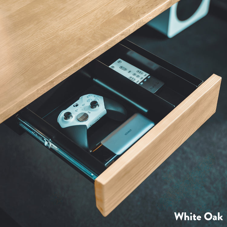 Minimalist Desky under-desk drawer in White Oak, open and showing a controller, remote, and power bank.
