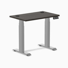 Desky Dual Mini sit-stand desk with burnished wood top, gray frame, and grommets.