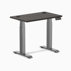 Desky Dual Mini sit-stand desk with burnished wood top, grommets, and space gray frame.