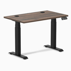 Desky Dual Mini sit-stand desk with Jarrah Legno top, matte black legs, and grommets.