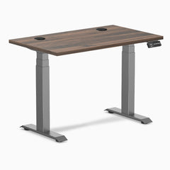 Desky Dual Mini sit-stand desk with Jarrah Legno top, Space Gray legs, and grommets.