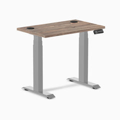 Desky Dual Mini sit-stand desk with natural walnut top, gray frame, and two grommets.