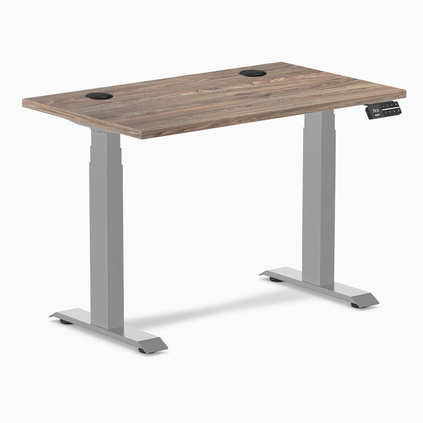 Desky Dual Mini sit-stand desk with natural walnut top, gray frame, and two grommets.