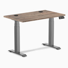 Desky Dual Mini sit-stand desk with natural walnut top, space gray frame, and grommets.