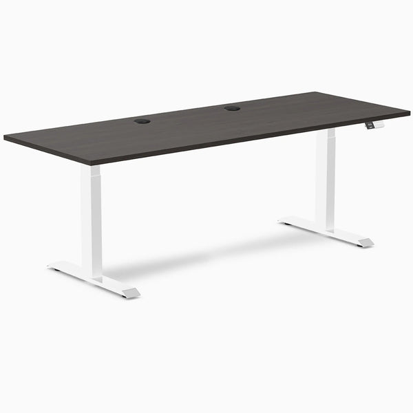 Desky Dual sit-stand desk with burnished wood laminate top, two grommets, and white frame.