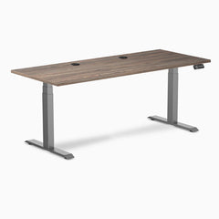 Desky Dual sit-stand desk with natural walnut laminate top, space gray frame, and two grommets.